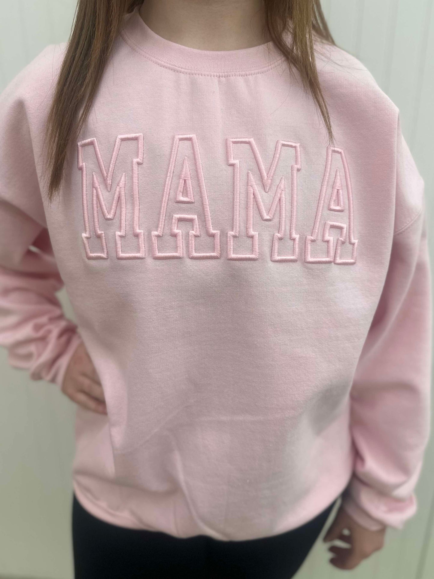 Model wearing pink sweatshirt that has MAMA embroidered in it