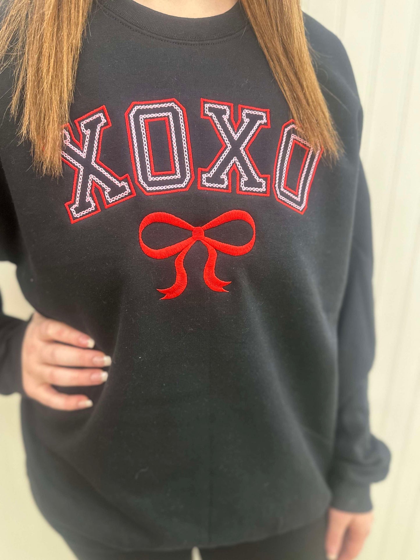 Model wearing avblack sweatshirt that has XOXO and a bow embroidered on it